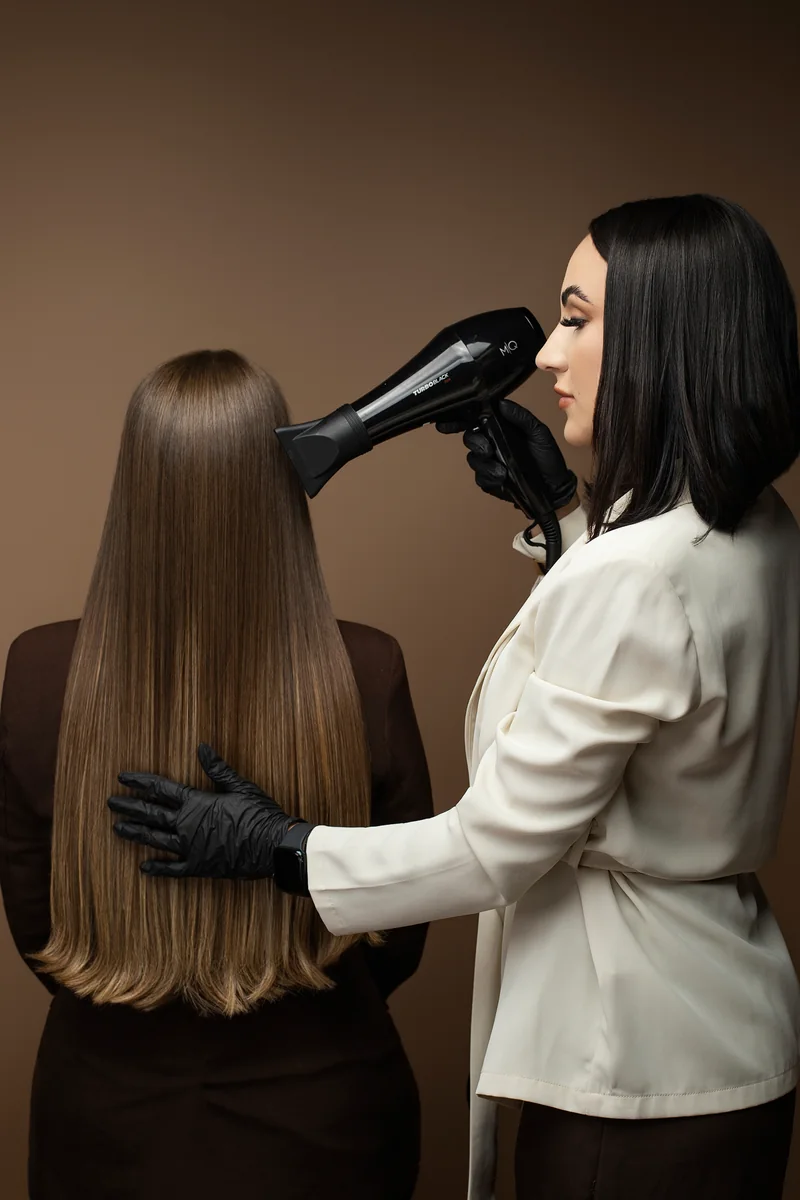 Luanna Martins finalizando com secador um cabelo longo e castanho